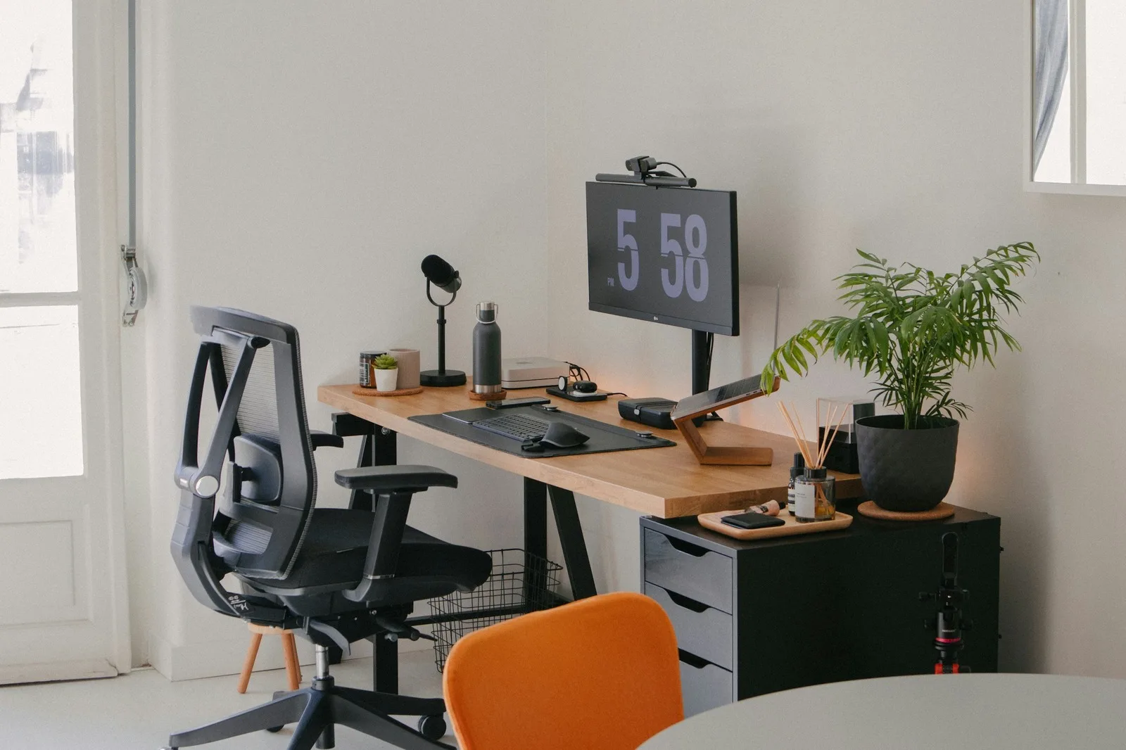 A tidy home office desk with a webcam mounted on top of a monitor, a desk lamp, a plant and an office chair