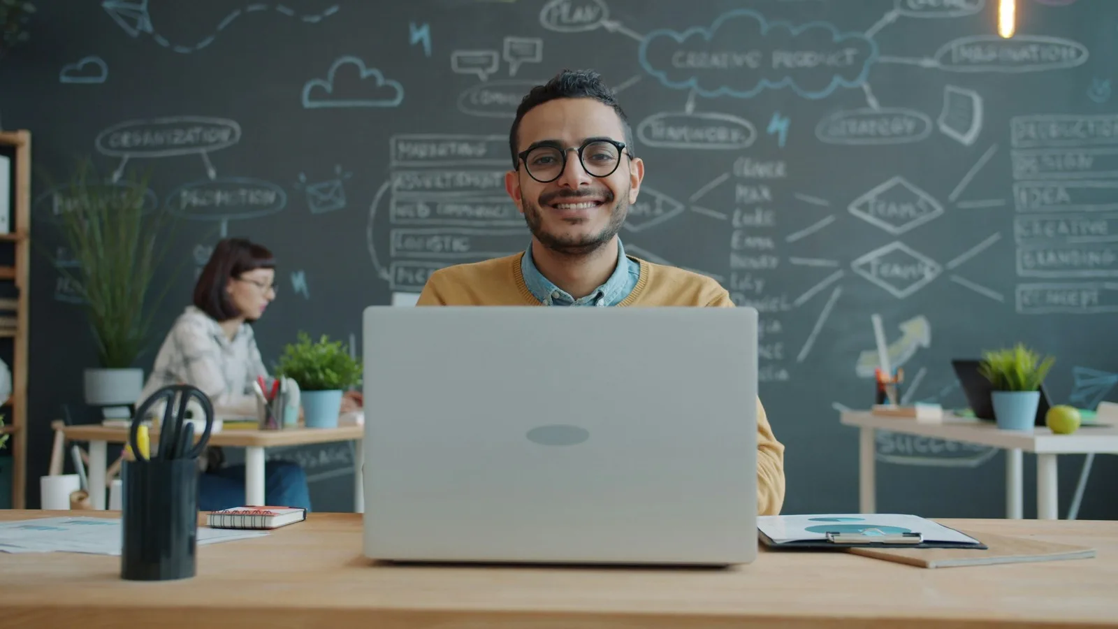 A man in glasses smiling straight into the camera over the top of his laptop