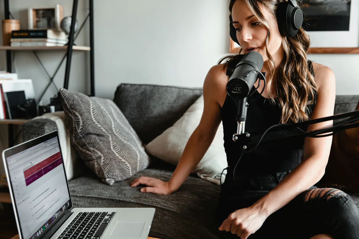 A woman with headphones speaking into a microphone on a boom arm next to her laptop