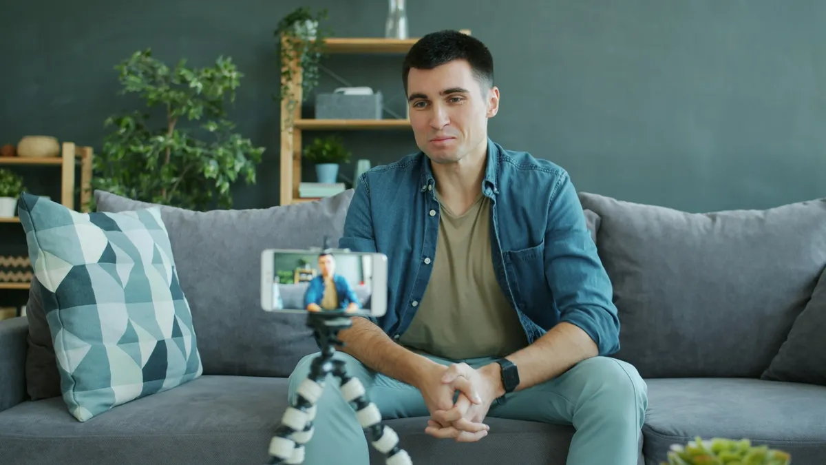 A man on a sofa recording himself on a phone on a small tripod