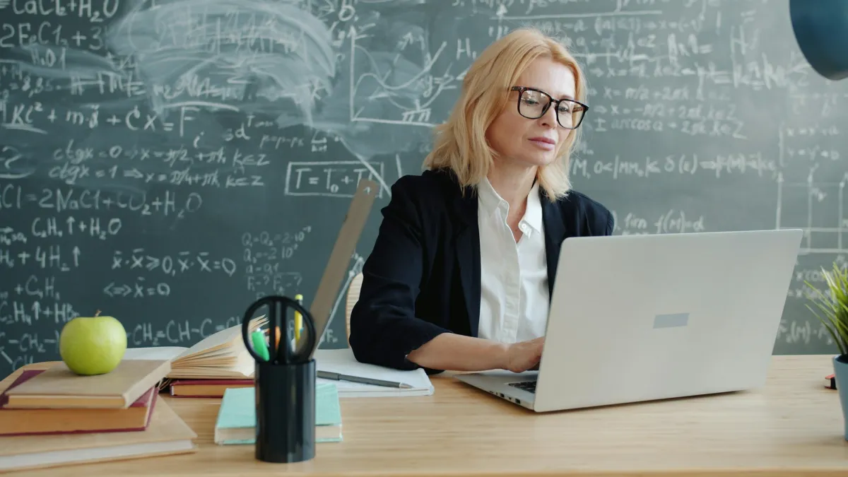 A teacher working at a laptop in front of a chalkboard