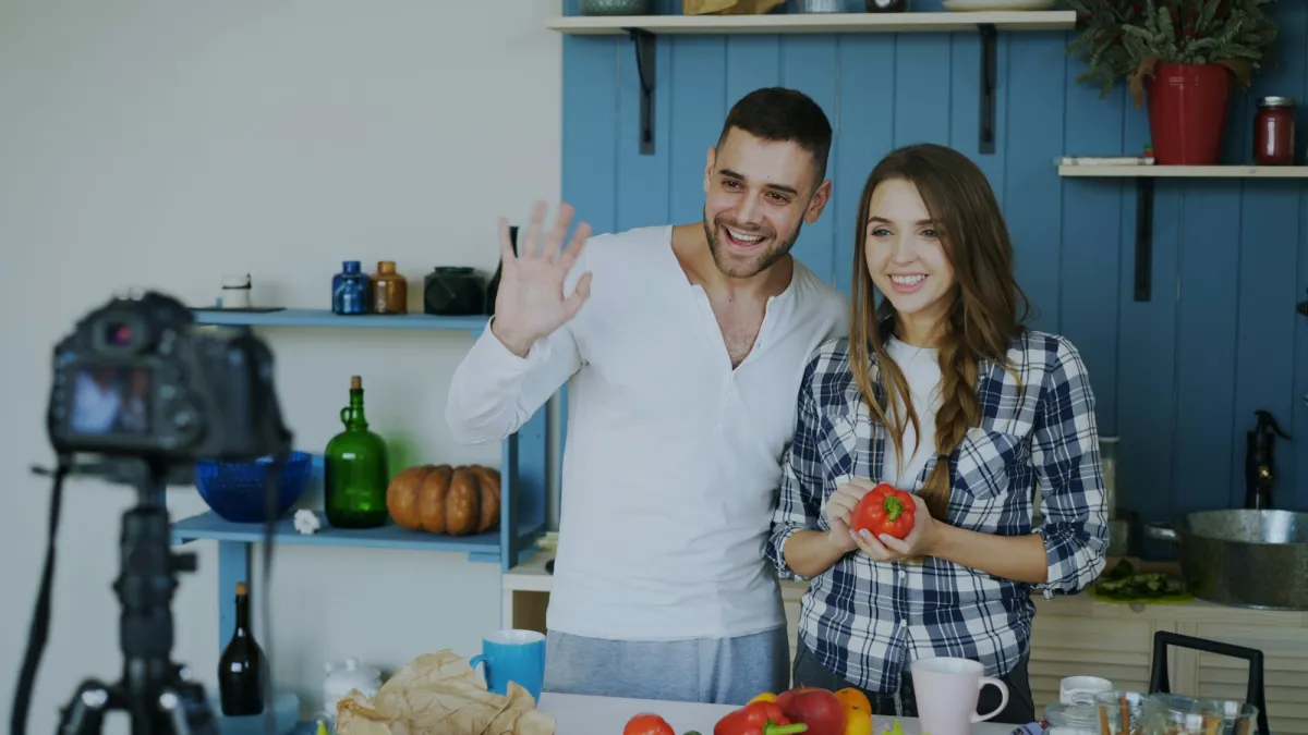 Two people waving at a camera in their kitchen