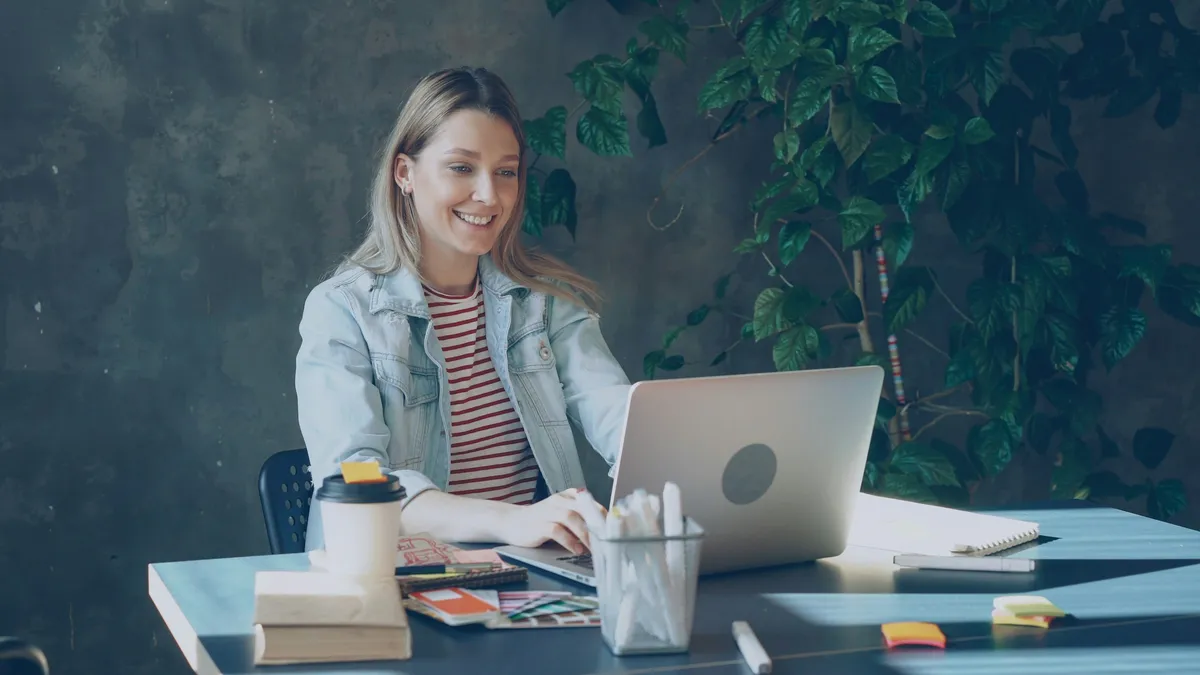 A smiling woman talking to her laptop at her desk