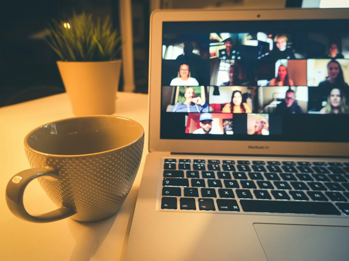A laptop showing a video meeting grid, beside a coffee cup