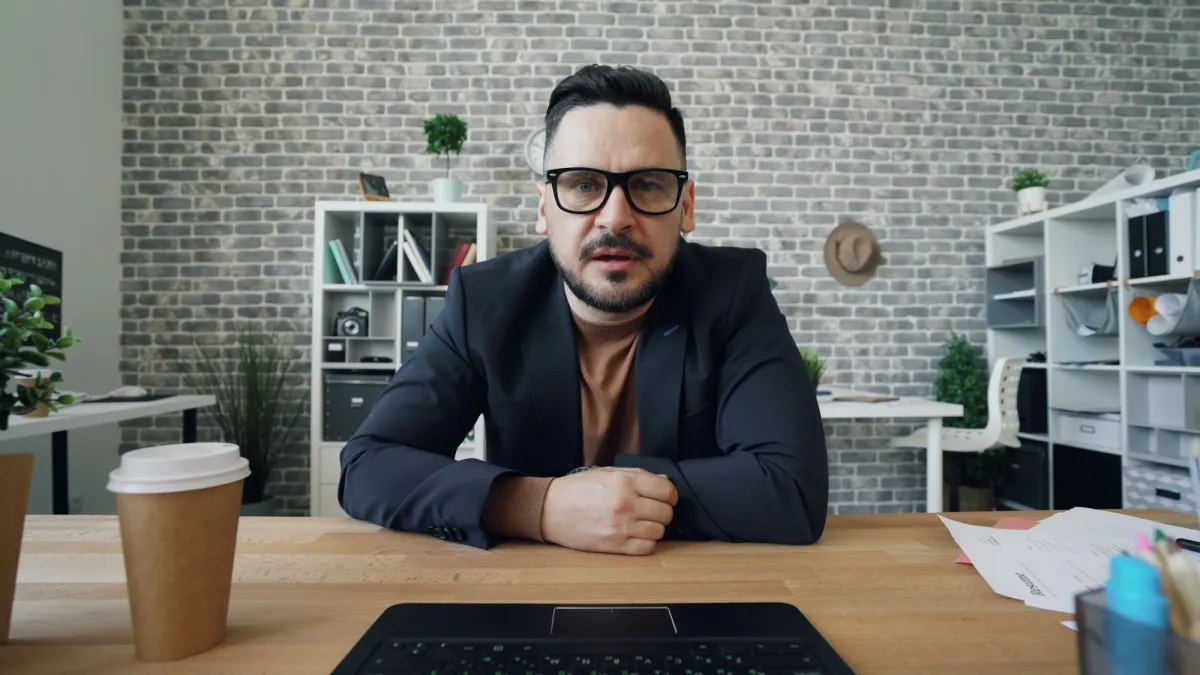 A man in glasses speaking to the camera from his desk