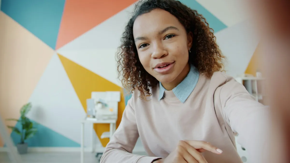 A young woman recording a self-tape in front of a colourful wall