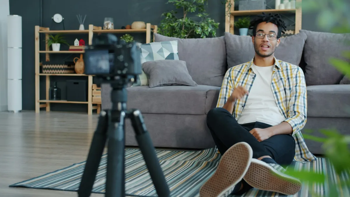 A man on his sofa recording a video on a camera on a tripod