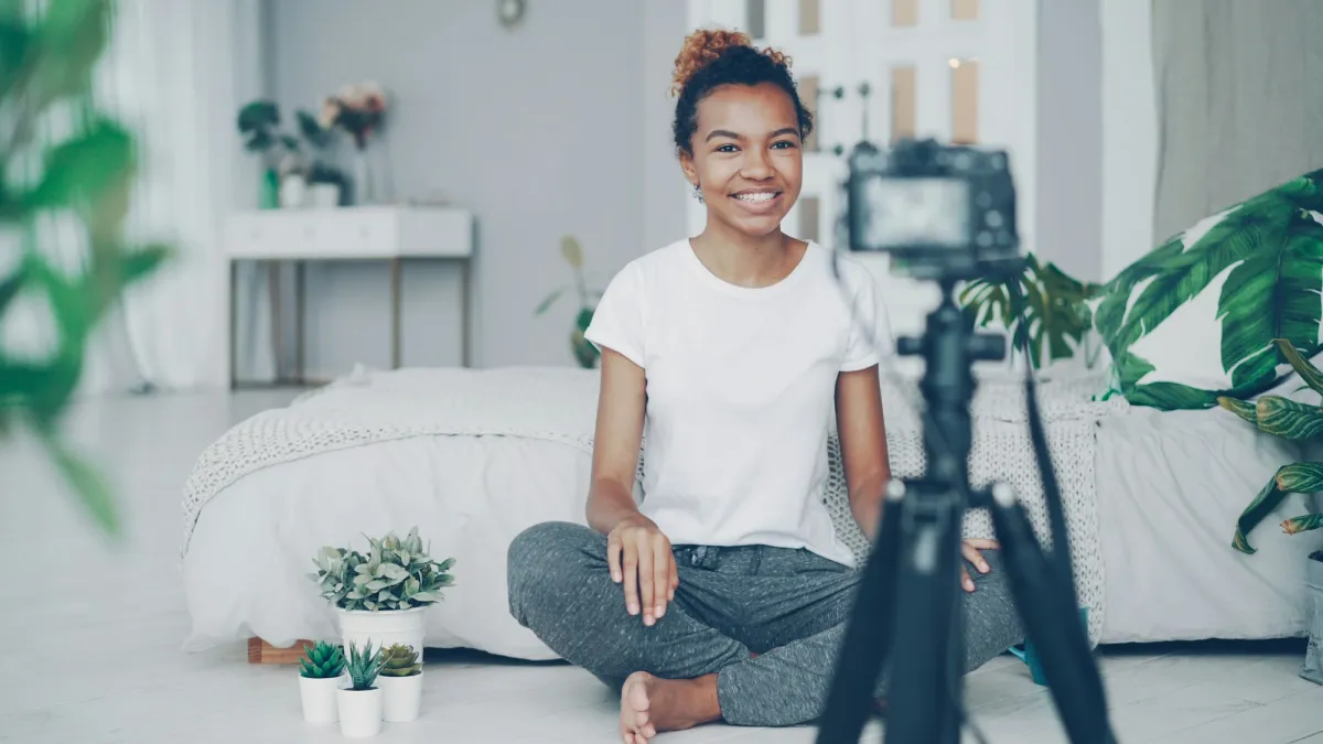 A woman sitting on her bed, recording a video on a camera on a tripod
